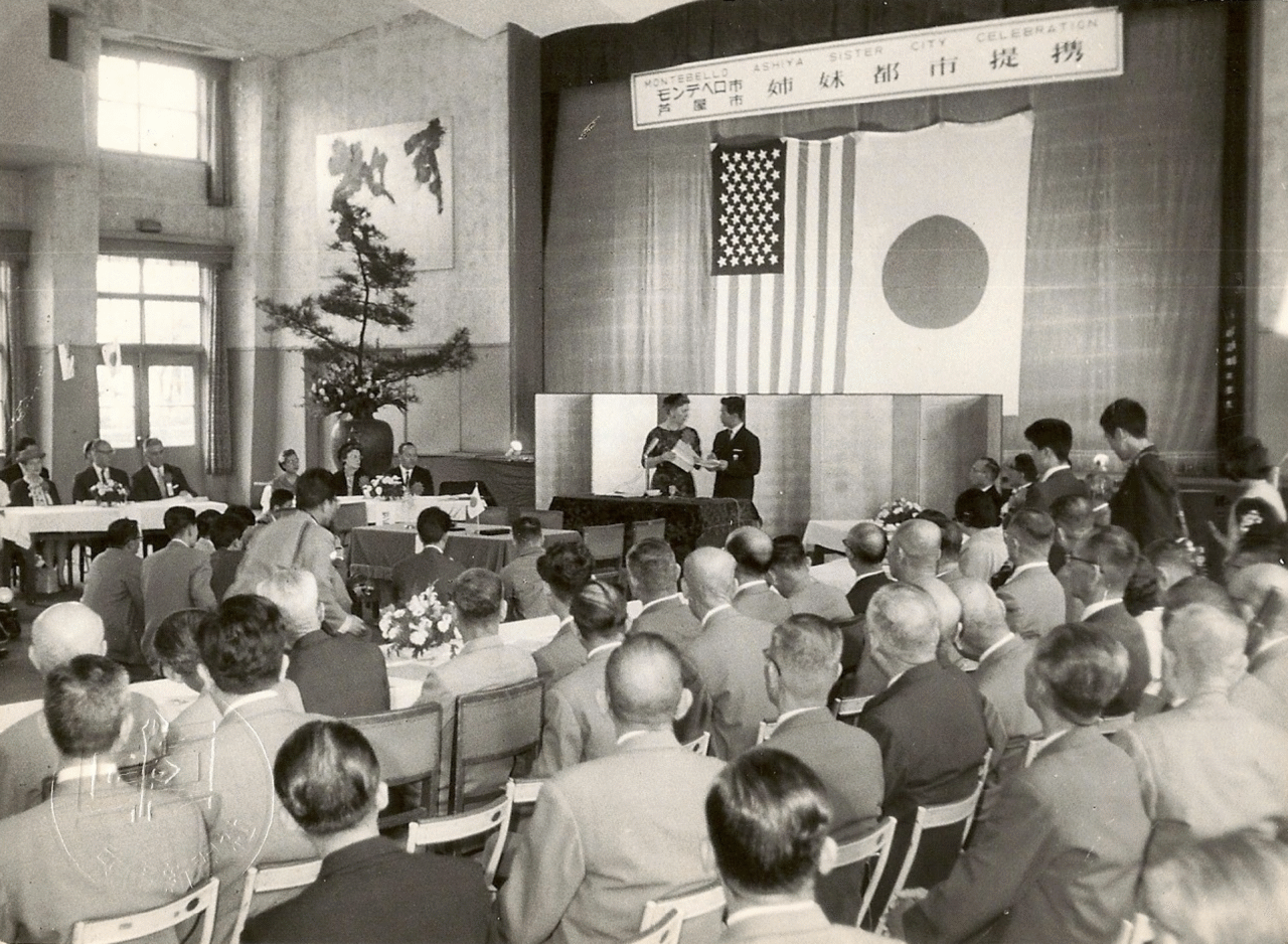 Guests attending the 1961 Montebello-Ashiya sister city signing ceremony beneath the flags of the United States and Japan